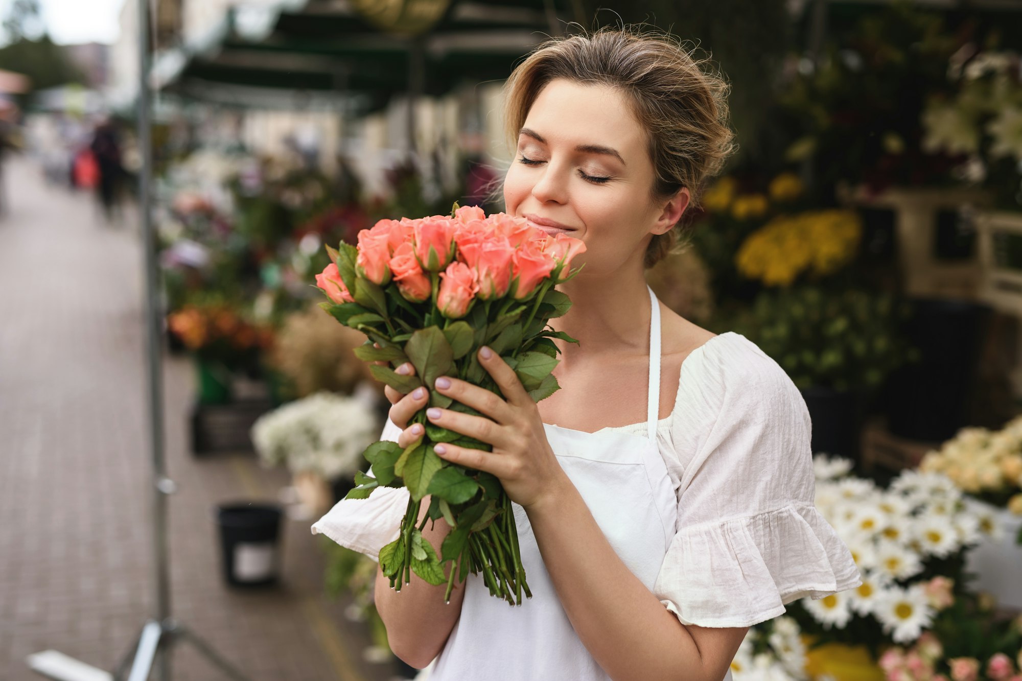 Woman florist with a heap of rose flowers in her little flower shop