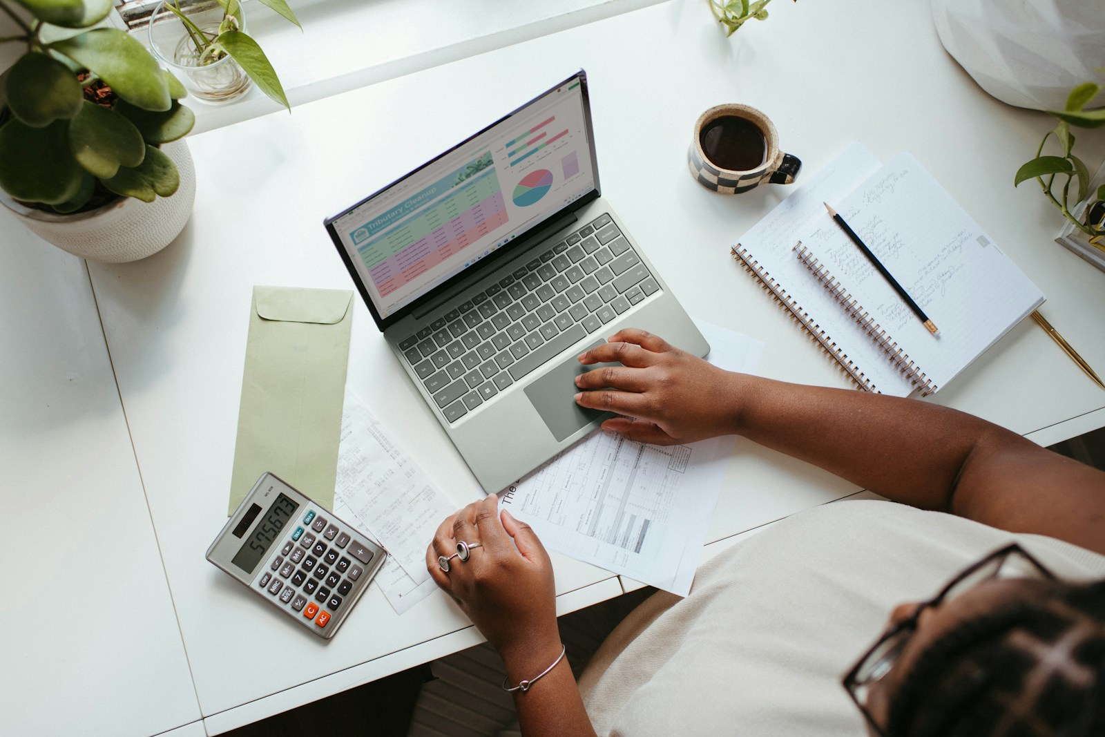 Woman comparing travel budgeting methods using envelopes and a laptop with a spreadsheet