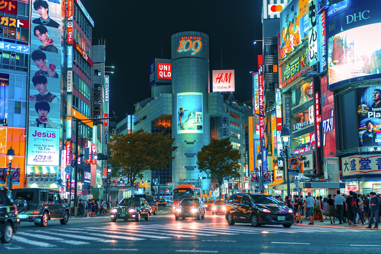 Crowded Shibuya Crossing at night with neon signs and pedestrians crossing the street