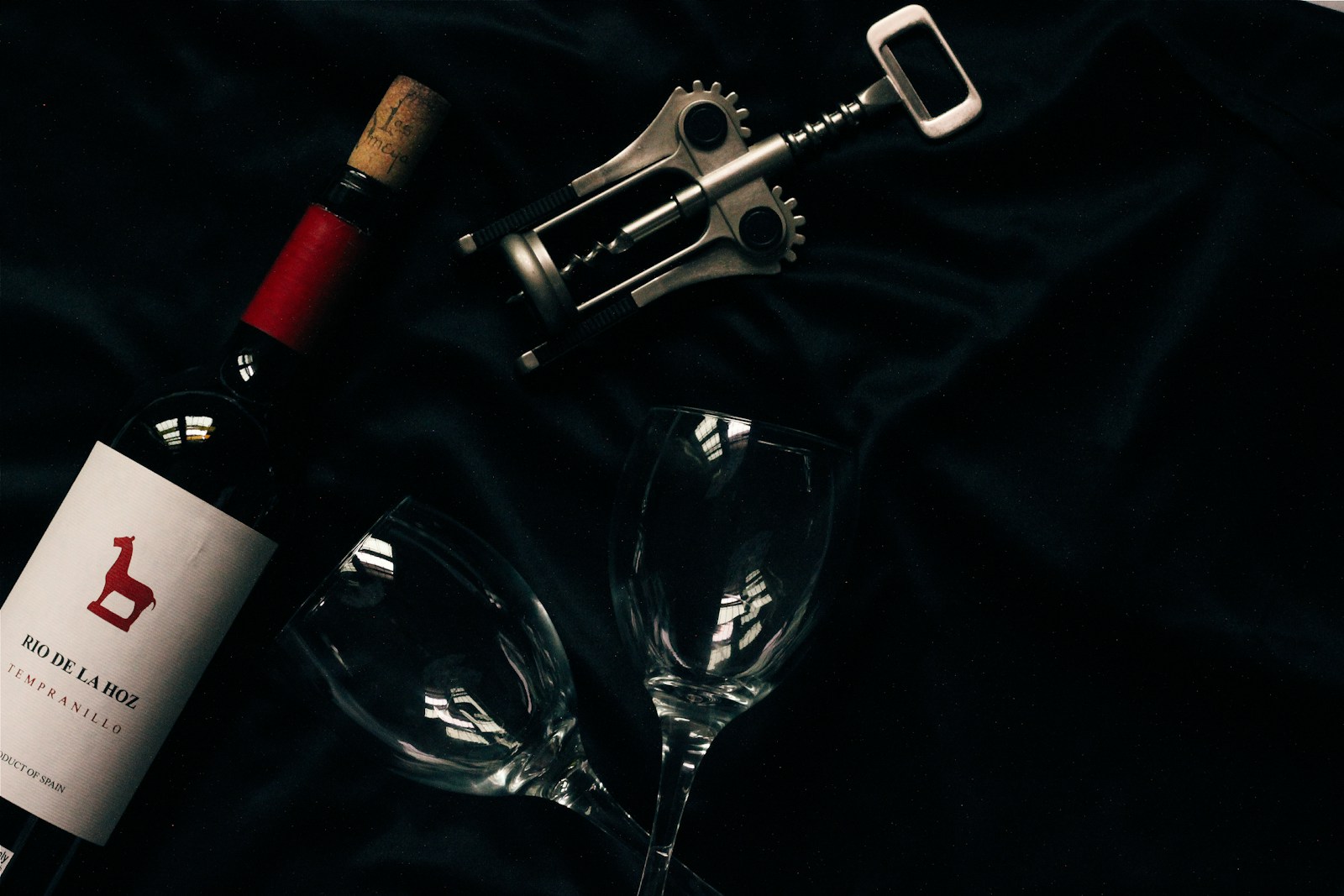 Flat lay of travel accessories including a wine tote bag, corkscrew, neck pillow, and sunglasses.