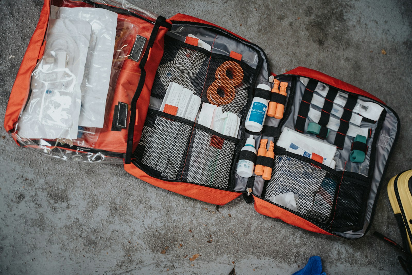 Open suitcase with a travel medical kit containing bandages, pills, and a first aid booklet inside a hotel room