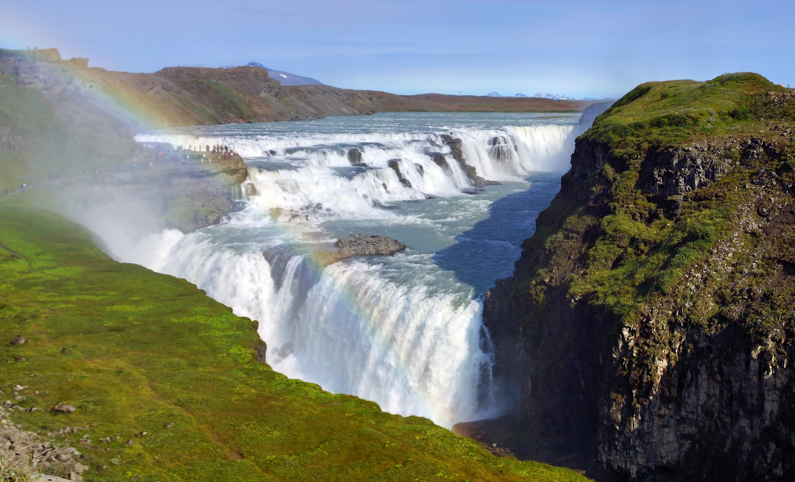 A powerful waterfall cascading down a cliff face in Iceland with a rainbow visible in the mist
