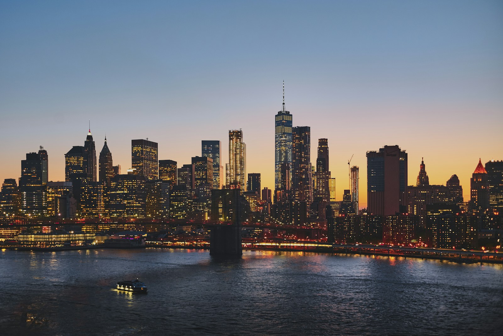 New York City skyline viewed from Brooklyn Bridge during sunset with warm golden light on buildings