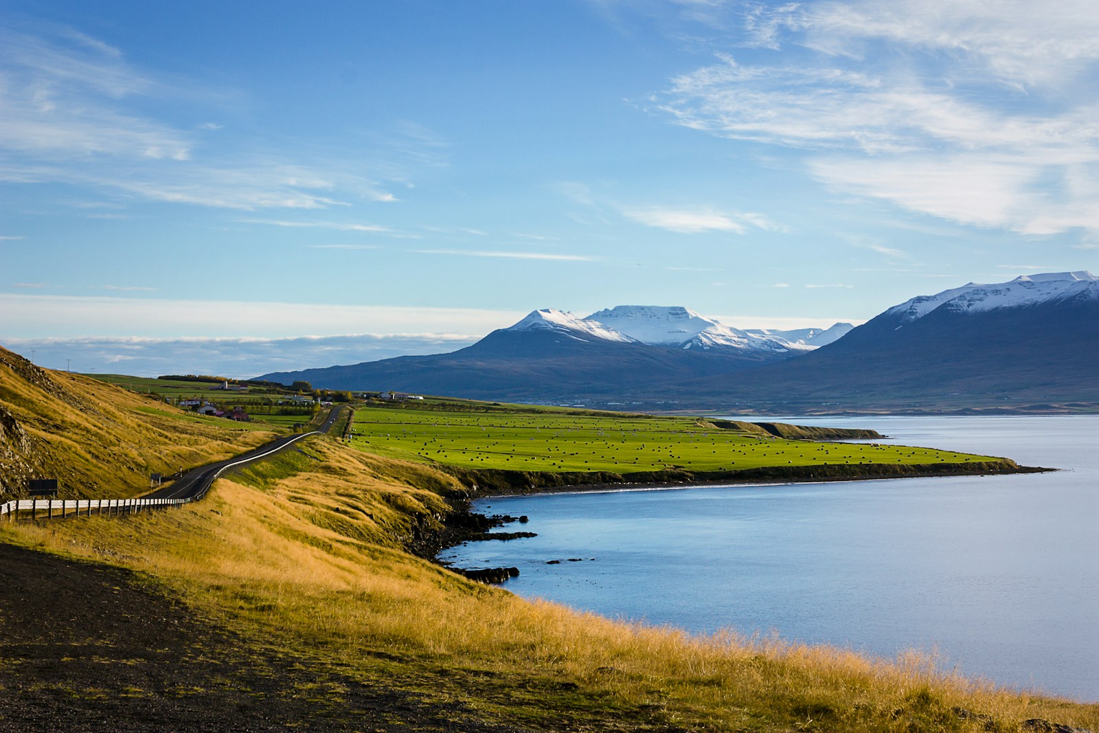 A hiker walking along a trail through a rugged Icelandic mountain landscape with green hills and a river