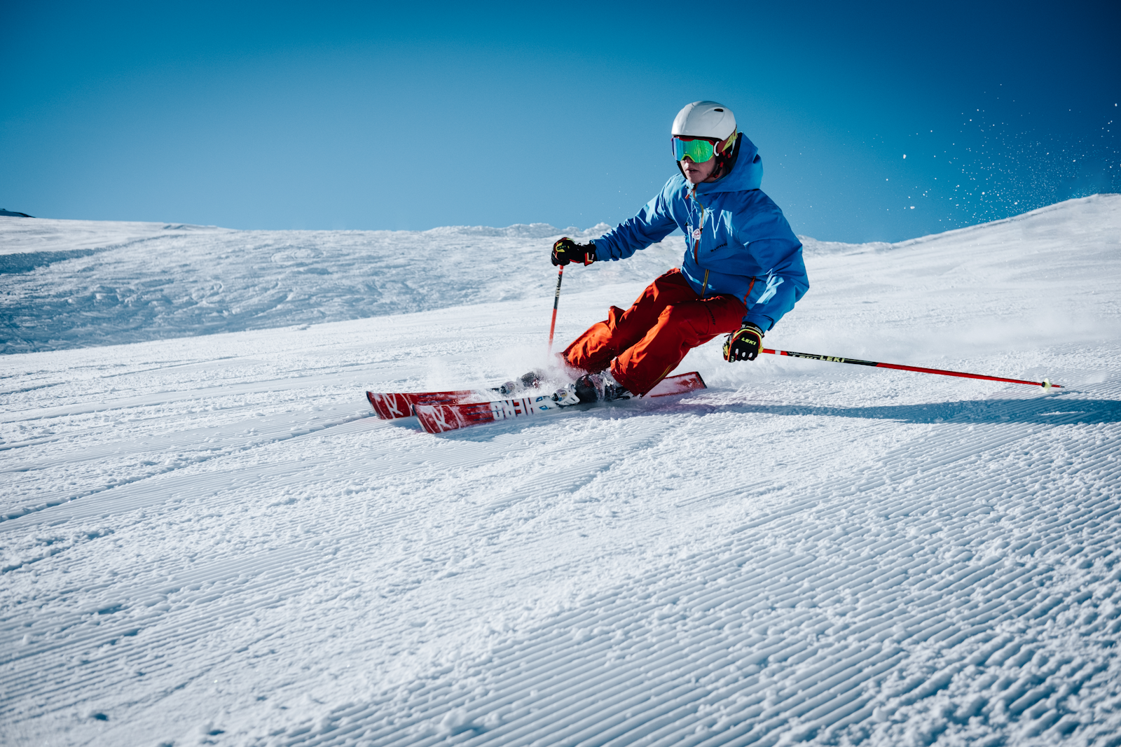 Ski gear including goggles, helmet, and gloves arranged on snow with mountain peaks in the background